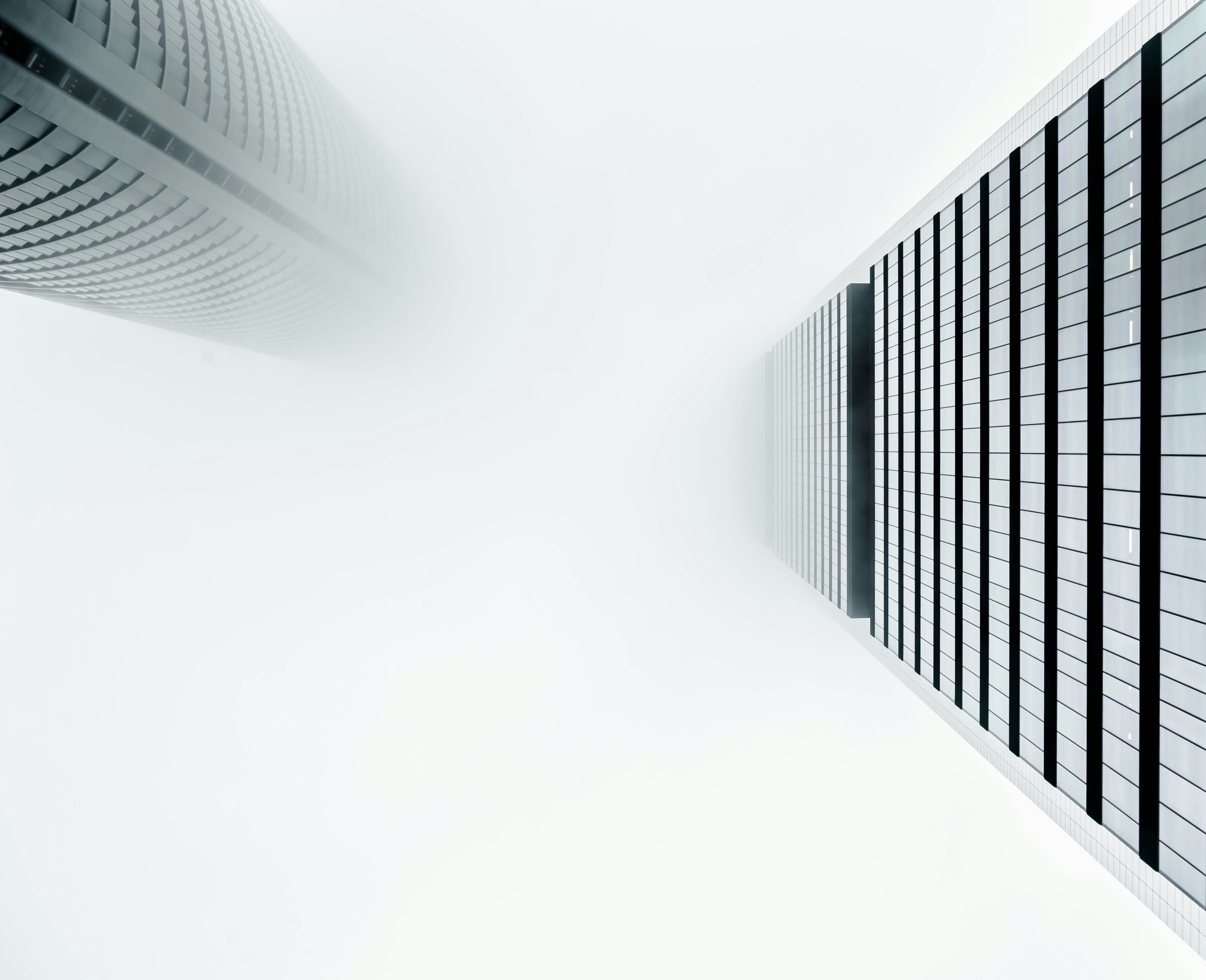 Two large glass towers side by side looking up from the ground and into the clouds